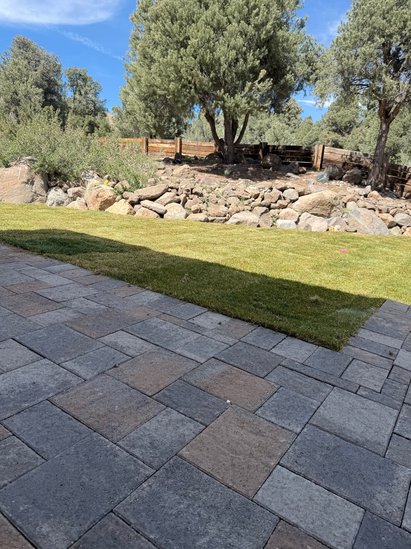 Paver patio meeting fresh sod with a natural rock border