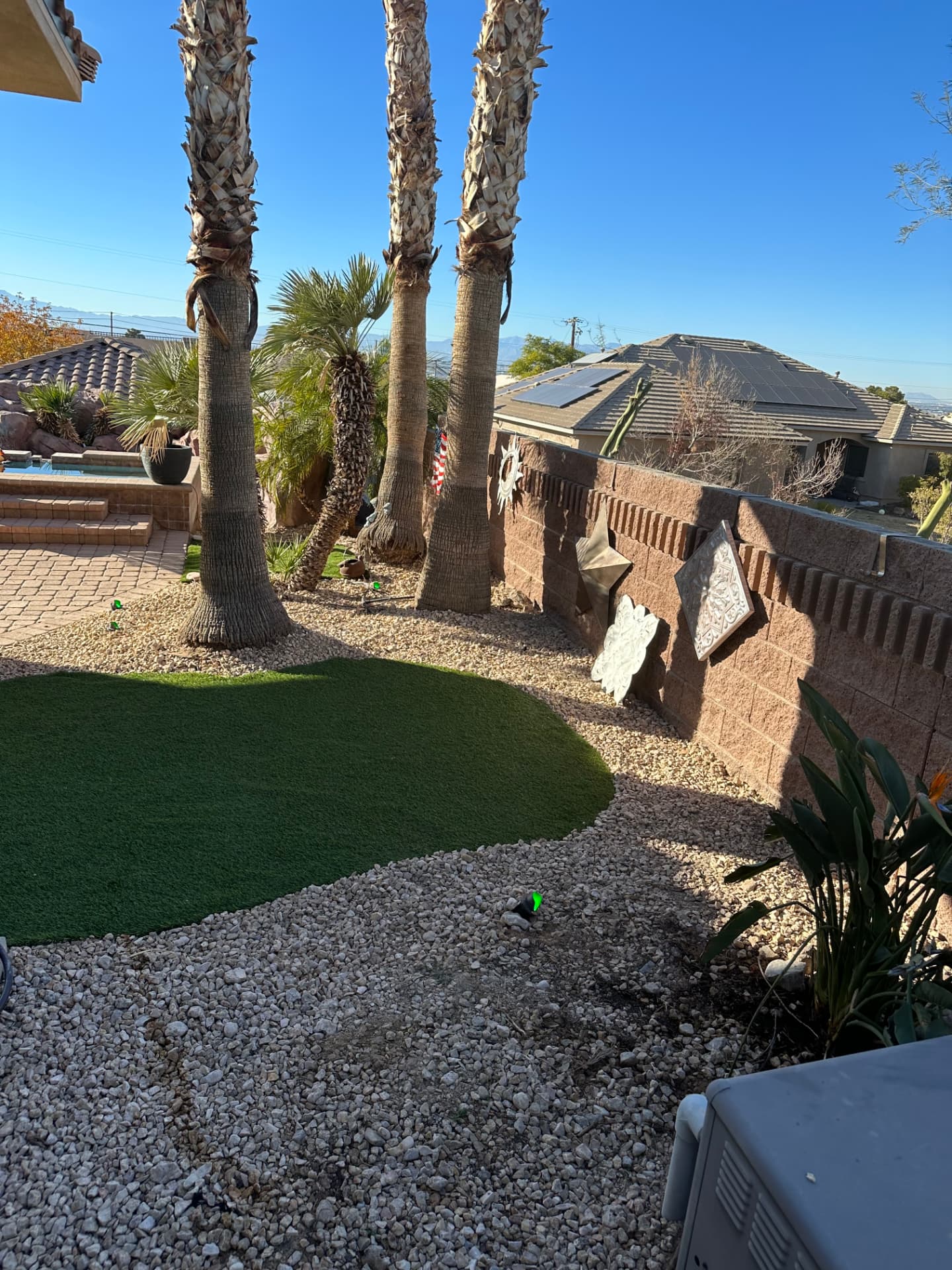 Curved turf lawn among palms with gravel beds along the block wall