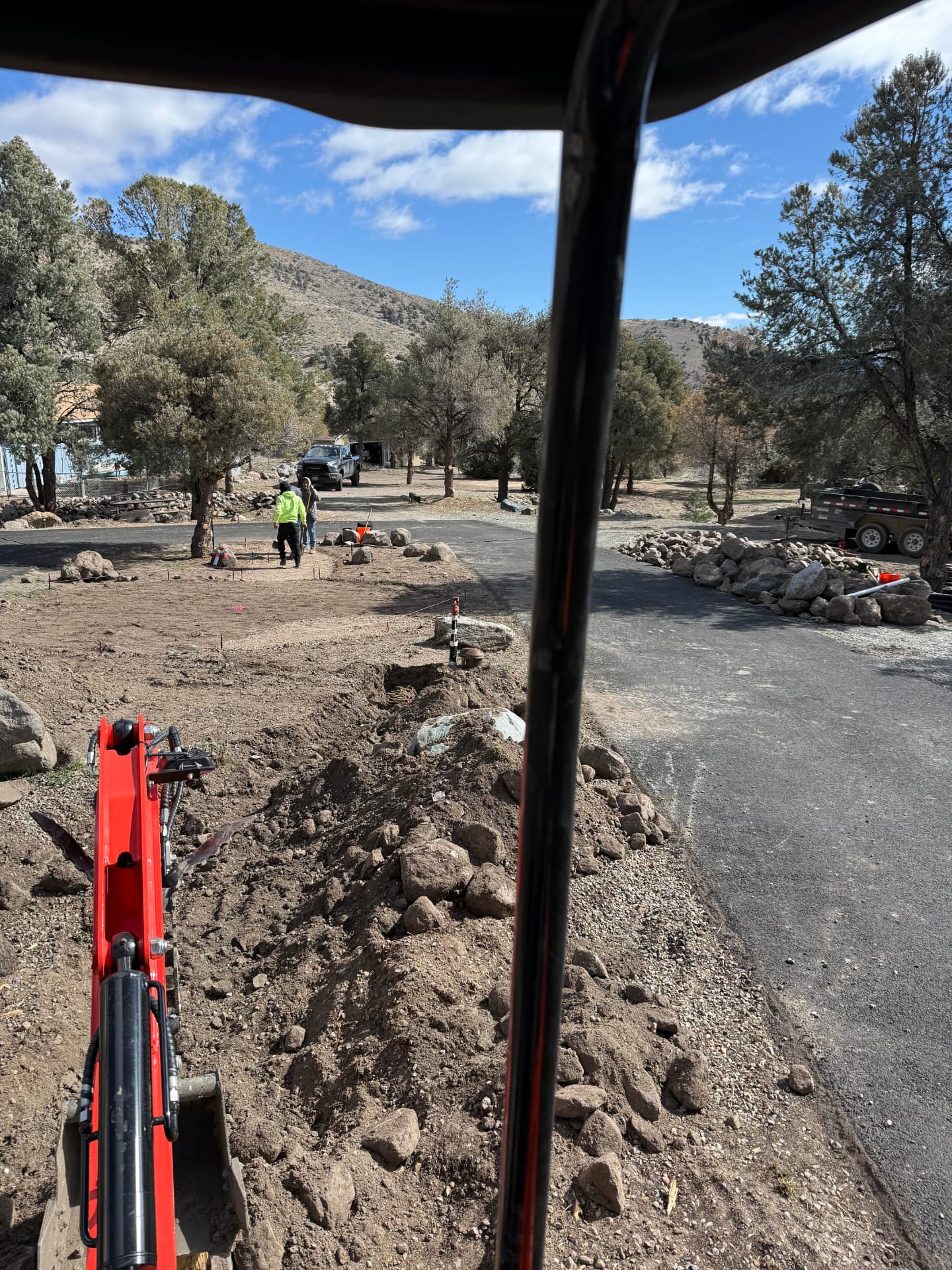 Operator view of trenching and layout stakes across the driveway island