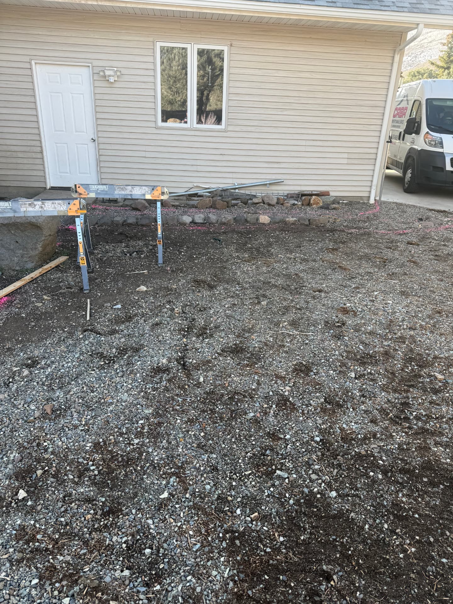 Dirt and gravel area beside the house marked out with pink paint before the patio install
