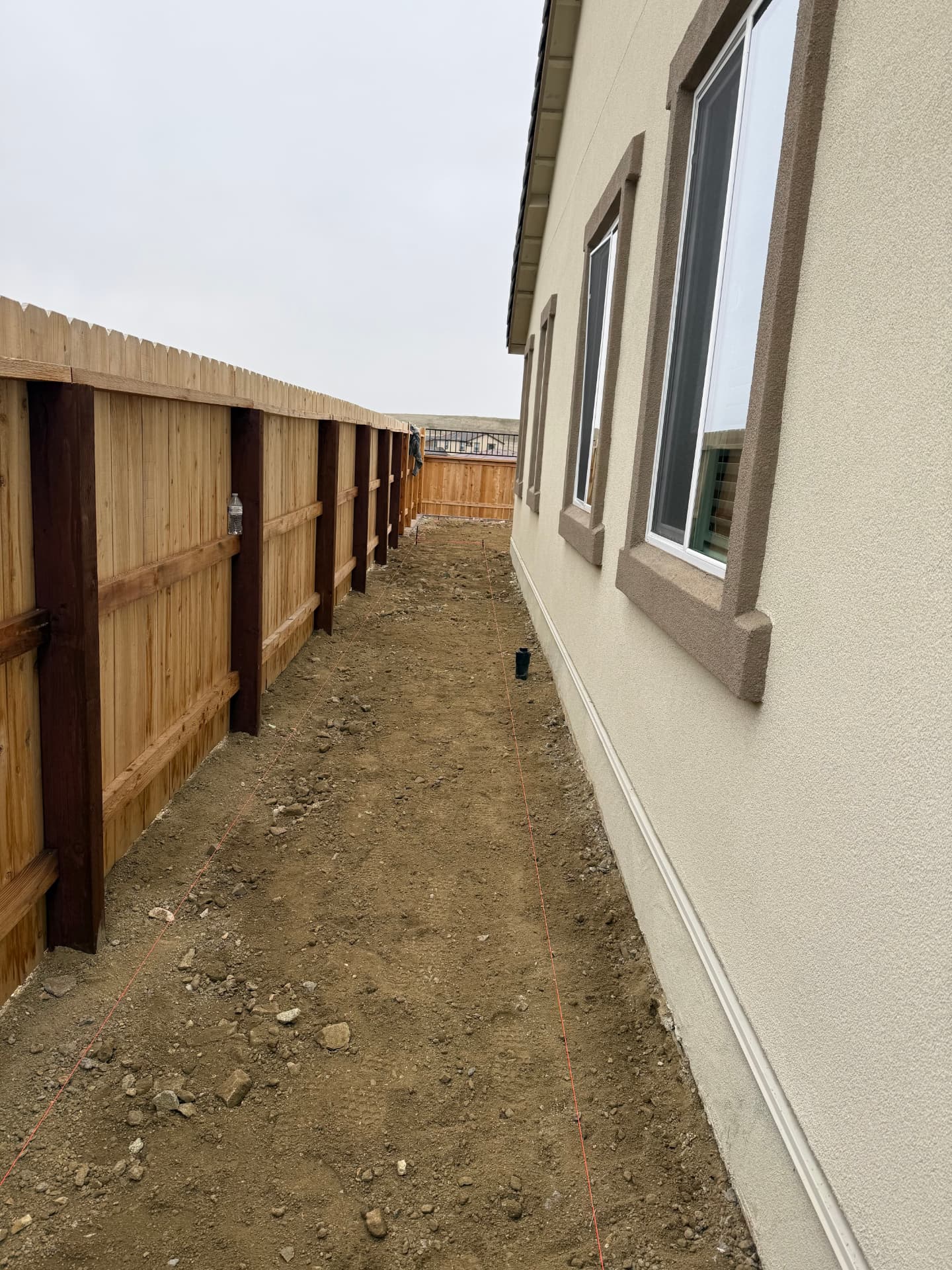 Narrow side yard dirt run with string lines set along the house