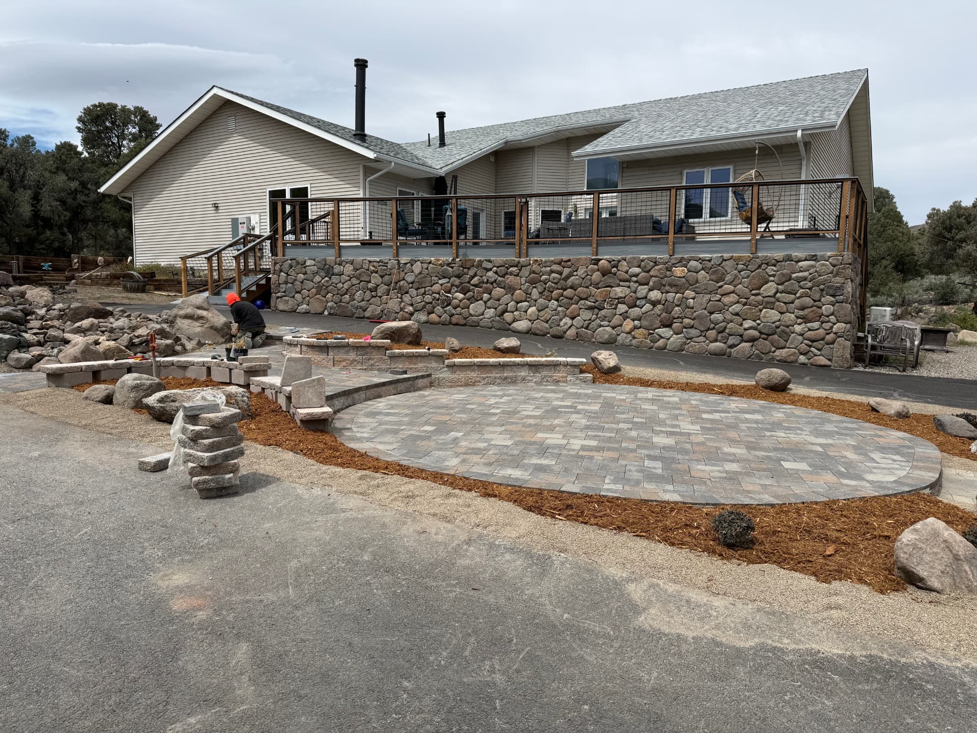 Completed oval paver patio, seat walls, and mulch beds below the stone deck wall