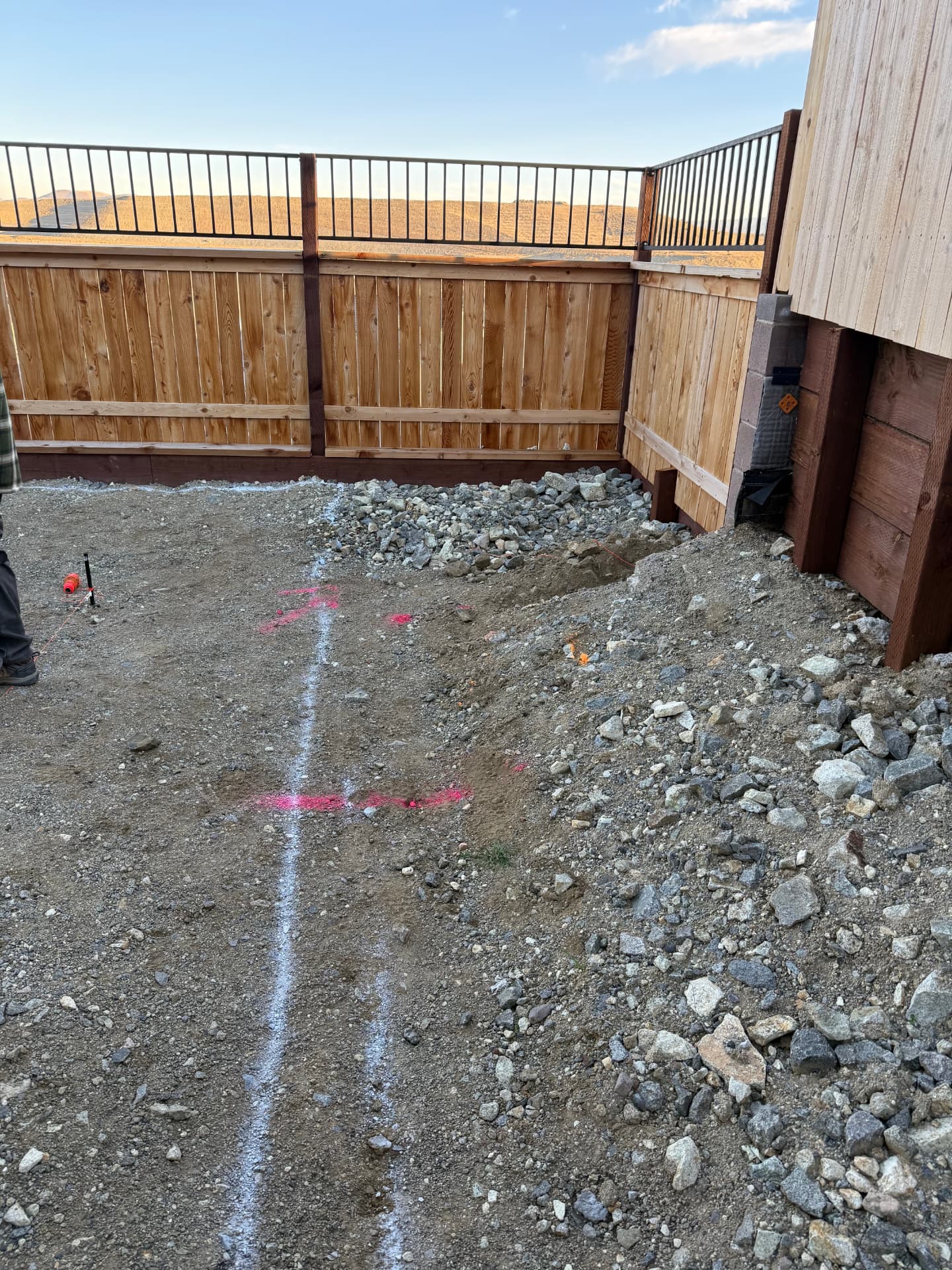 Backyard corner with spoil piles and layout lines against new fencing