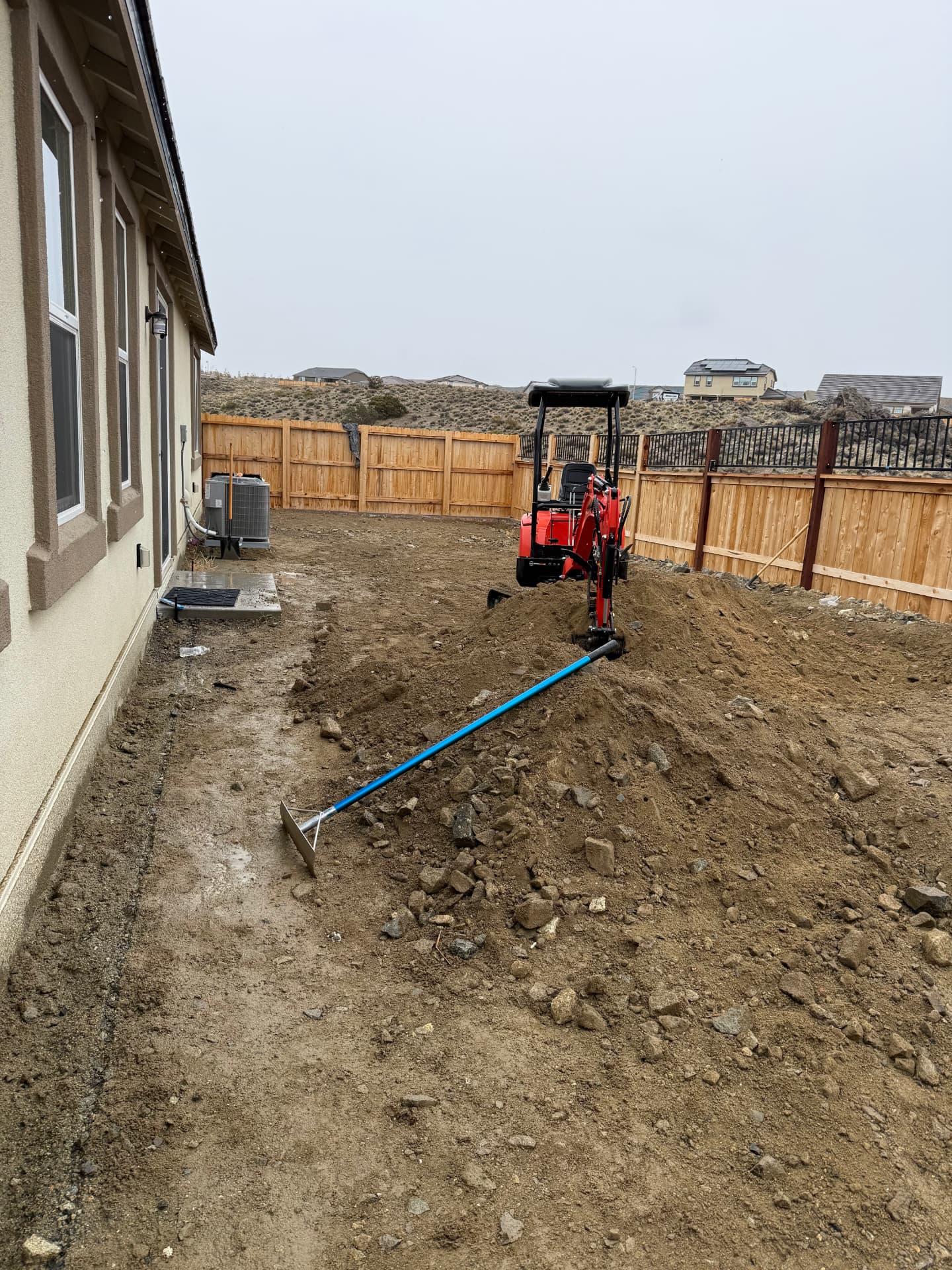 Mini excavator cutting grade in the bare backyard before construction
