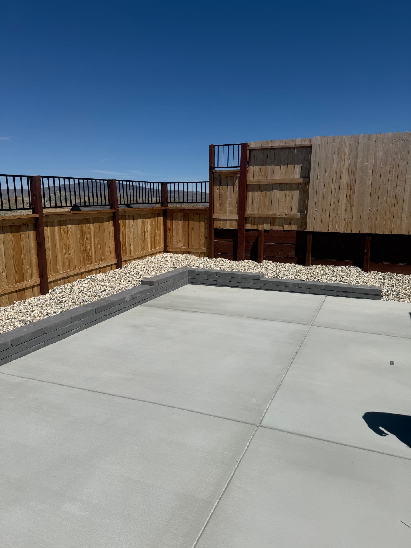 Completed patio slab with charcoal paver wall and white rock beds