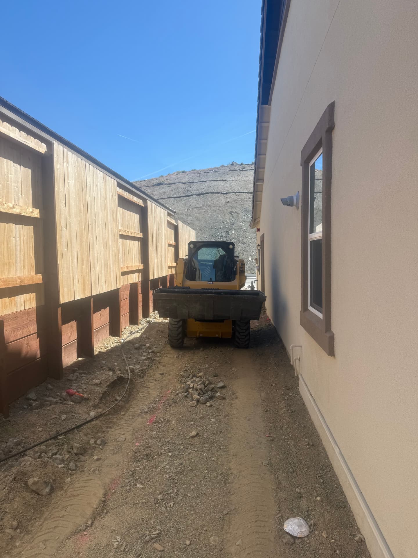 Skid steer hauling material through the side yard along the retaining wall