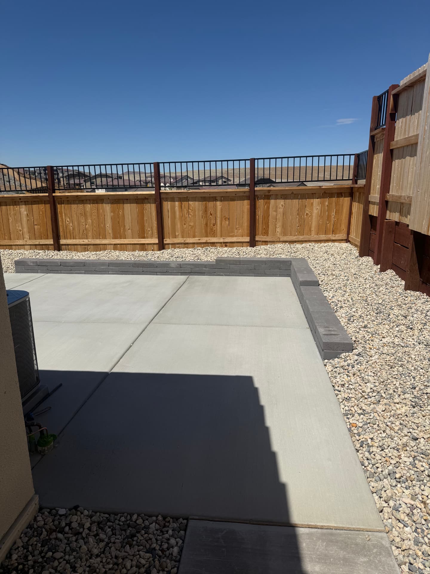 Finished backyard concrete patio with paver seat wall and rock border