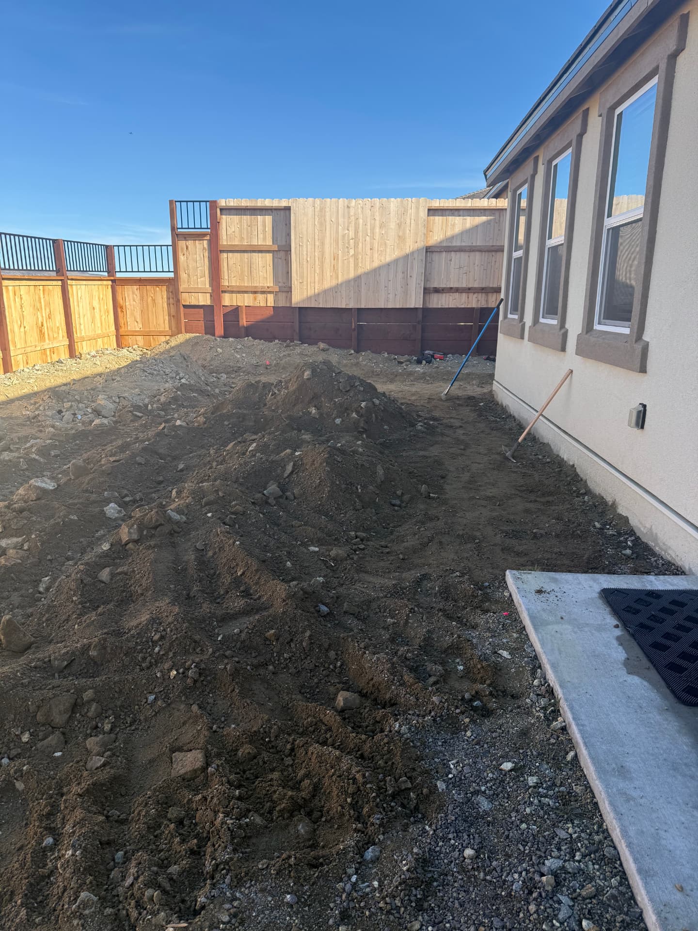 Backyard graded dirt and rock piles against a new cedar fence before hardscaping