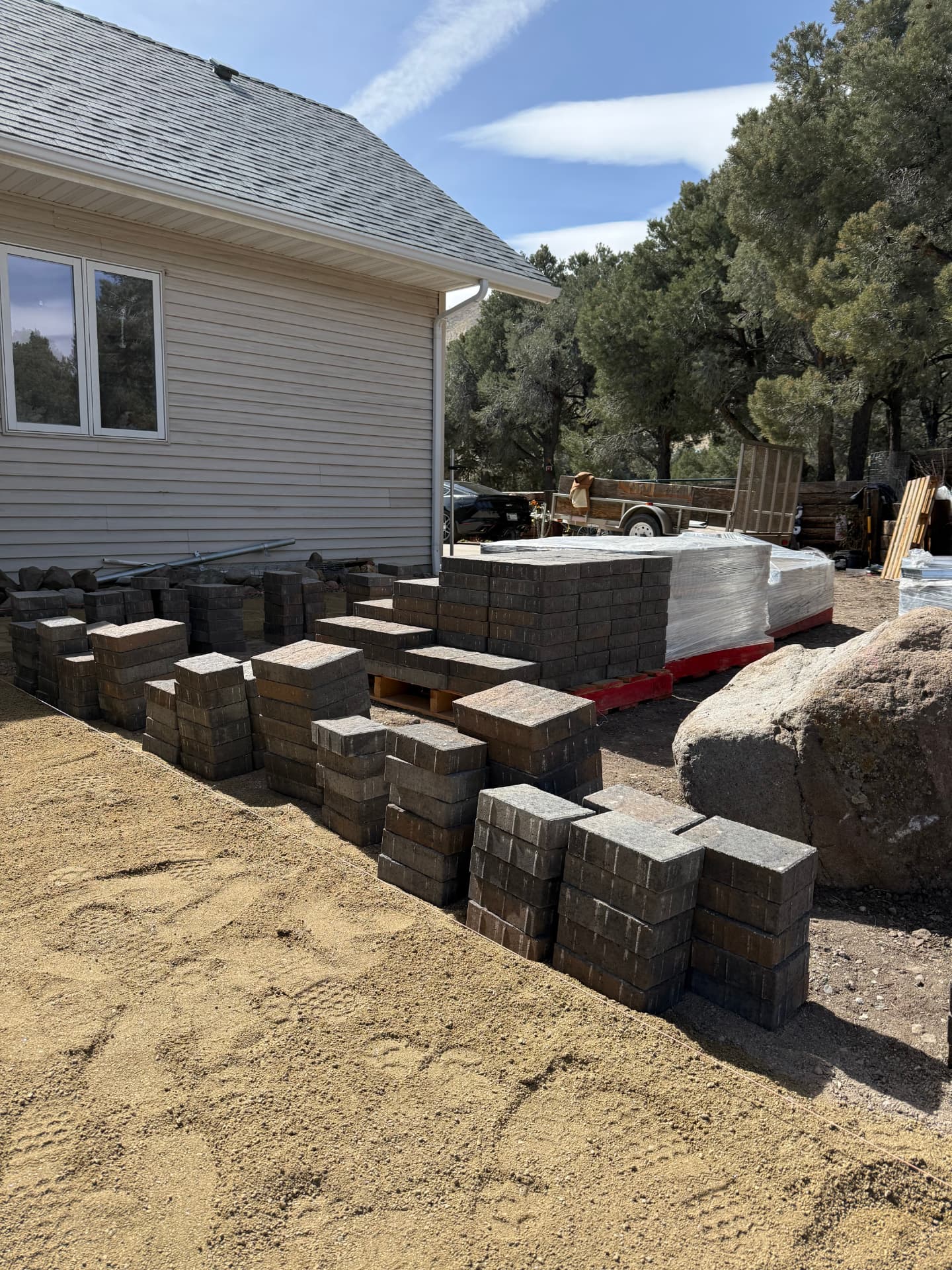 Stacks of pavers and wall block staged next to the leveled sand base