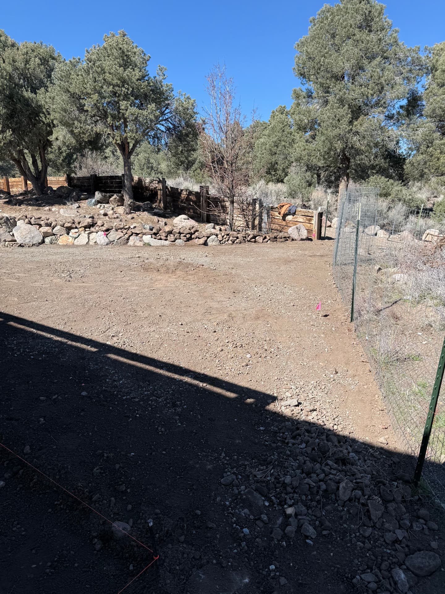 Dirt yard with rock border and wood fencing before the project begins