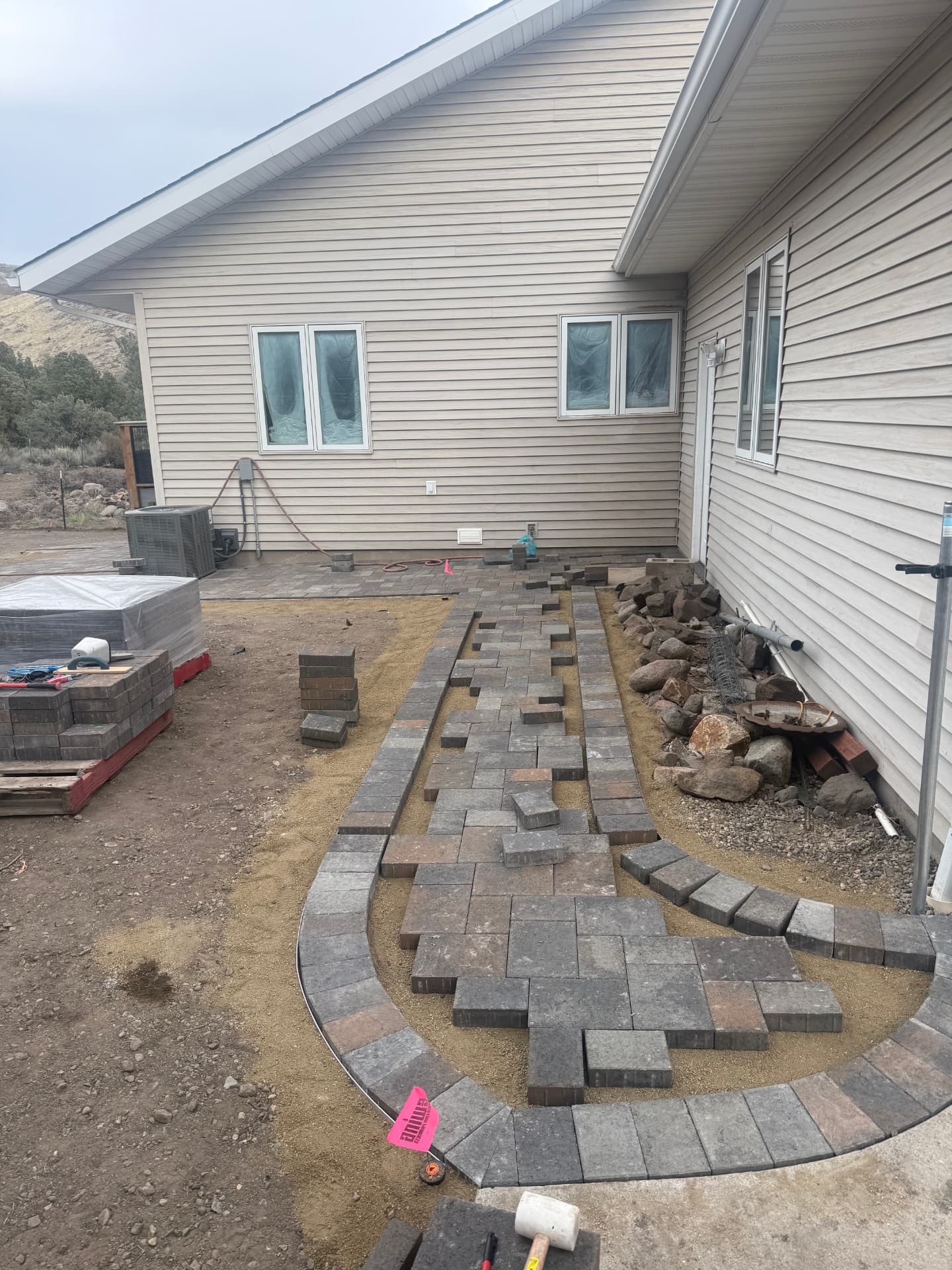 Curved paver walkway being laid along the back of the house
